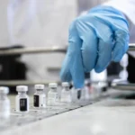 gloved hand selecting vax vial 0 0